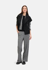 Zwarte gestructureerde jas met brede revers, gelaagd over een grijze top. Grijze gestreepte wijde broek en zwarte chunky boots maken de outfit af.