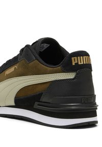 Sneakers PUMA con tomaia in suede nero e oliva, dettagli beige e suola bianca a contrasto. Logo dorato distintivo sul tallone e sul lato.