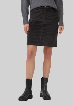 Zwarte corduroy rok met knoopsluiting aan de voorkant, knielang, gecombineerd met zwarte enkelboots met een chunky zool. Grijze trui zichtbaar aan de bovenkant.