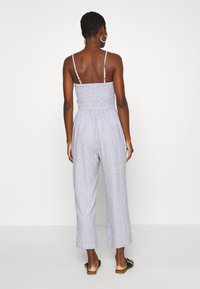 Gestreepte jumpsuit met smock-borstel, dunne banden, wijde benen en lichte stof. Kleur: blauw en witte strepen.