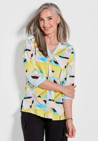 Bunte Bluse mit geometrischem Muster aus leichtem Stoff. Verfügt über einen V-Ausschnitt, Dreiviertelärmel und kontrastierende hellblau Akzente.