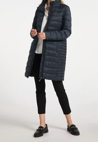 Granatowa puchowa kurtka z ukośnym pikowaniem, wysokim kołnierzem, przednim zamkiem błyskawicznym i bocznymi kieszeniami. Połączona z czarnymi, skróconymi spodniami i mokasynami.