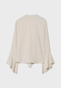 Blouse crème à manches longues avec des poignets évasés et volantés, et un ourlet droit, vue de dos sur un fond blanc uni.