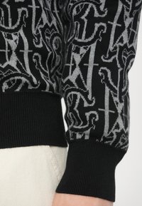 Maglione nero con motivo astratto grigio. Polsini e orlo a coste. Tessuto morbido a maglia, dettaglio ravvicinato della manica.