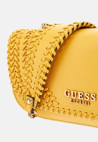 Borsa gialla con dettagli di cuciture testurizzate, caratterizzata da una finitura liscia e un logo in rilievo color oro. Composta in materiale sintetico.