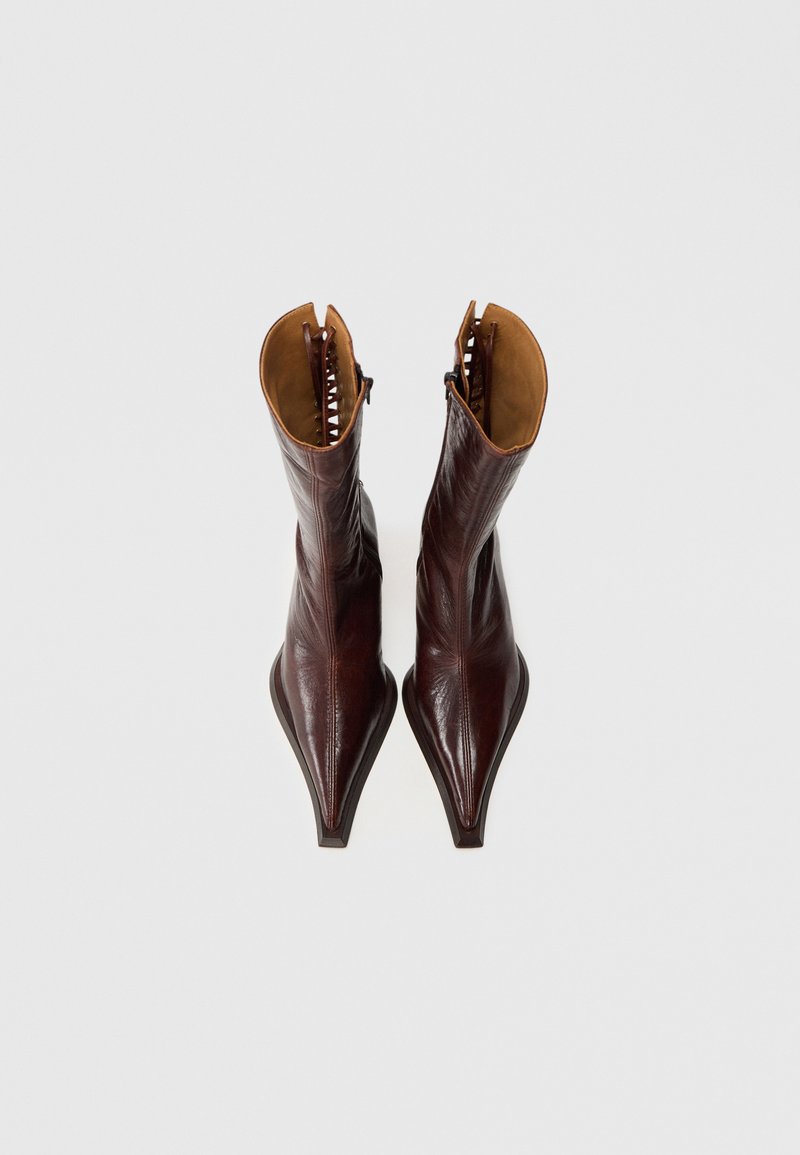 Bruine leren enkellaarsjes met puntige neuzen, gladde afwerking en een contrasterende tan binnenvoering. Voorzien van een zijrits en decoratieve stiksels.