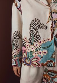 Buttoned cream shirt and pants with colorful zebra and floral prints, showing a person's hand and part of the outfit's sleeve.