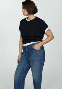 Schwarzes kurzärmliges Hemd mit weißen Manschetten, kombiniert mit hochgeschnittenen blauen Jeans. Einfaches Design, klare Linien und baumwollähnliche Textur.