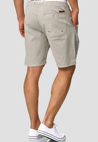 Shorts en coton gris clair avec une poche arrière, dotés de deux boutons et d'un accent en cuir marron. Longueur en dessous du genou avec une coupe décontractée.