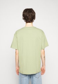 T-shirt vert clair à manches courtes avec un col rond, texture douce et coupe ample. Présente un petit logo près de l'épaule.