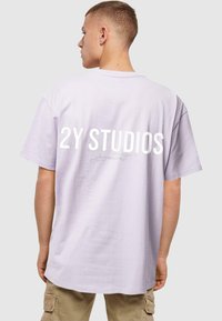 Šviesiai purpurinė medvilninė marškinėlių priekyje, su ryškiu baltu užrašu "2Y STUDIOS" ant nugaros. Laidus kirpimas, trumpomis rankovėmis ir apvaliu iškirpimu.