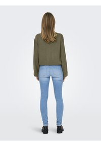 Maglietta a maniche lunghe verde oliva con un fit rilassato, abbinata a jeans skinny bleu chiaro, dotati di tasche posteriori e una discreta texture in denim.