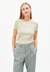 T-shirt fitted verde chiaro a maniche corte, abbinato a pantaloni a vita alta grigi a righe con chiusura a bottone e tasche laterali.
