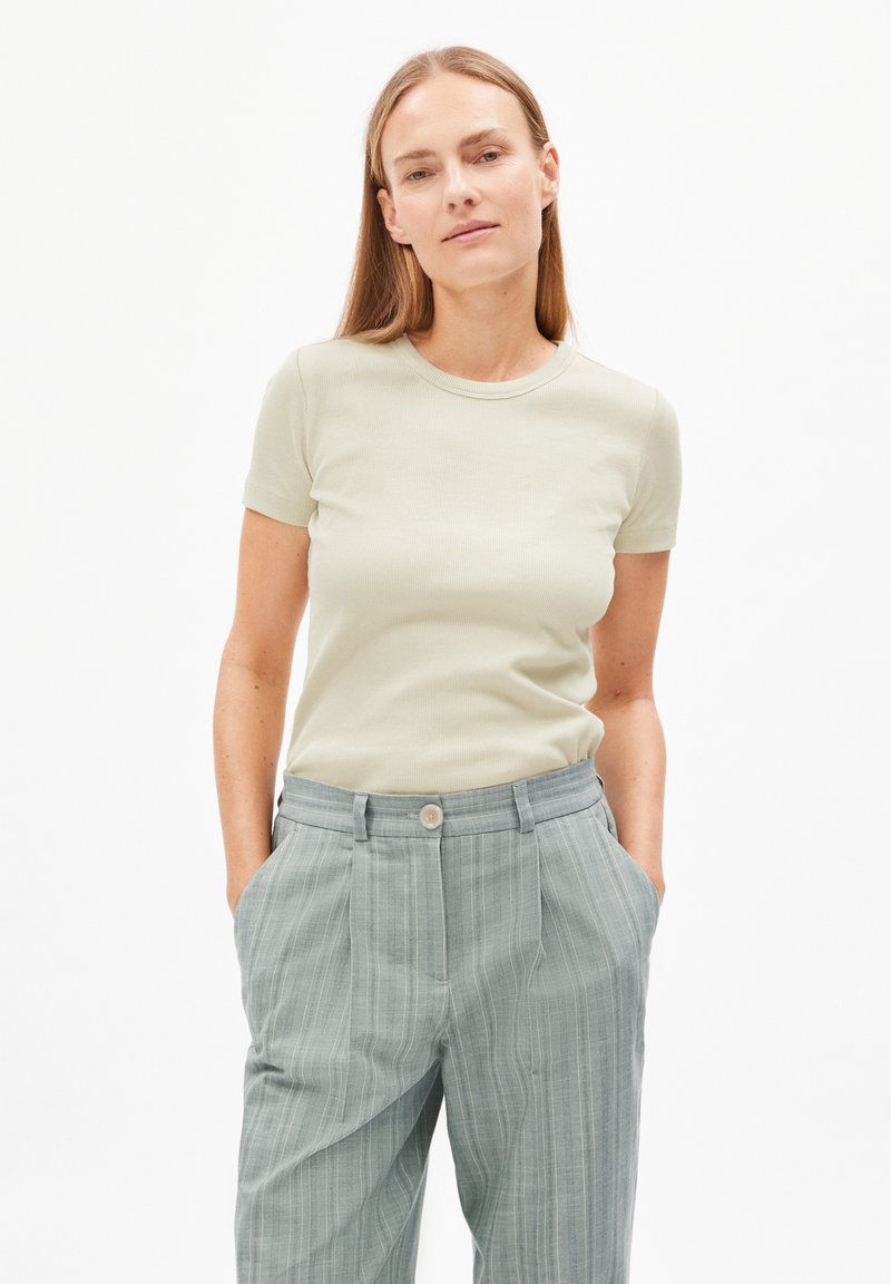 T-shirt fitted verde chiaro a maniche corte, abbinato a pantaloni a vita alta grigi a righe con chiusura a bottone e tasche laterali.