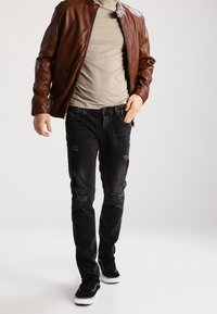 Brun läderjacka, ljusgrå t-shirt, slitna svarta jeans med lagningar, och svarta sneakers med vita sulor. Avslappnad outfit.