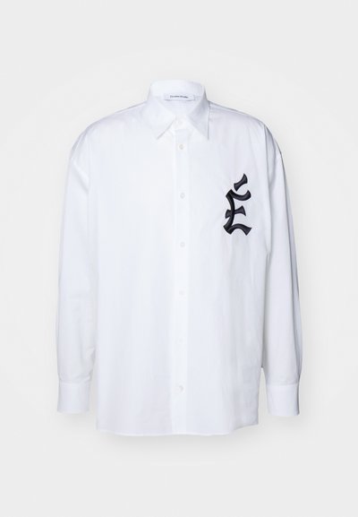 Λευκό πουκάμισο με κουμπιά και μακριά μανίκια, φτιαγμένο από λεία ύφασμα. Διαθέτει ένα μαύρο κεντημένο λογότυπο στο αριστερό στήθος και κλασικό γιακά.