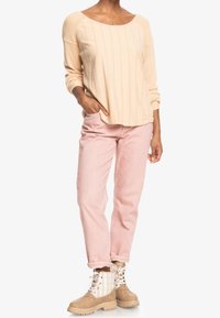 Haut côtelé beige à manches longues associé à un pantalon droit rose pastel et des bottines marron clair avec un motif à damier sur les côtés.