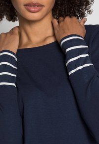 Mörkblå långärmad topp med rundad halsringning, featuring randiga manschetter i vitt och mörkblått. Mjuk tyg med avspänd passform.