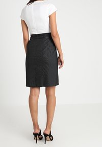 Haut blanc à manches courtes associé à une jupe noire ajustée, présentant un motif texturé et une fente à l'arrière. Des chaussures noires à talons hauts complètent le look.