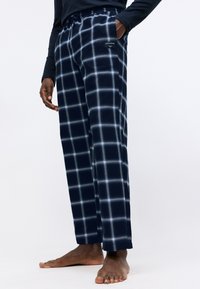 Navy karirane lounge hlače od mekanog materijala, sa strukom na vezanje i bočnim džepovima, s bijelim linijama koje stvaraju motiv.