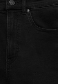 Gros plan sur la poche avant d’un jean en denim noir avec un bouton visible et des détails de rivets sur un tissu solide.