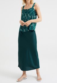 Turkos, blommönstrad ärmlös topp med breda axelband, kombinerad med en lång, enfärgad turkos kjol. Texturerad tyg och sandaler med remmar fulländar looken.