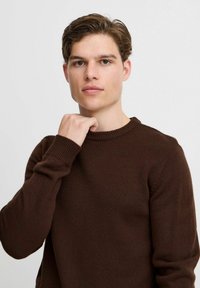 Brauner Strickpullover mit rundem Halsausschnitt und gerippten Ärmelbündchen, der über eine glatte Textur und eine taillierte Passform verfügt.