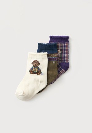 Drei Paar Knöchelsocken in Weiß mit einem Teddybär, olivgrün mit Mustern und violett kariert, übereinander auf einem hellen Hintergrund angeordnet.
