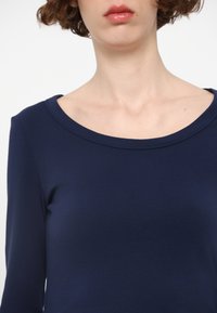 Marineblaue Langarmbluse mit rundem Ausschnitt und glatter Textur. Der Stoff wirkt weich und anliegend, was den Ausschnitt und die Schultern betont.