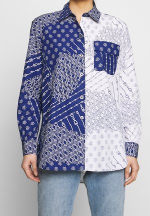 Langærmet skjorte med knapper i kontrasterende navyblå og hvide geometriske og kædermønstre, båret med lyseblå jeans.