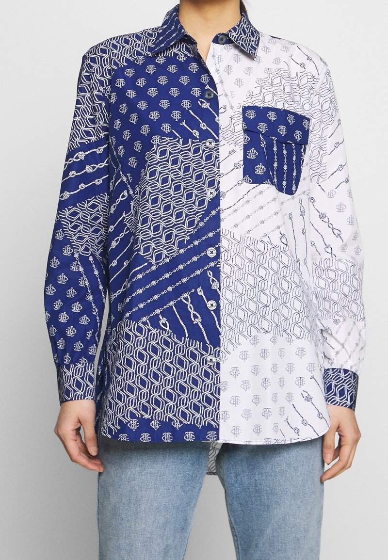 Chemise à manches longues boutonnée avec motifs géométriques et chaînes bleu marine et blanc contrastants, portée avec un jean bleu clair.