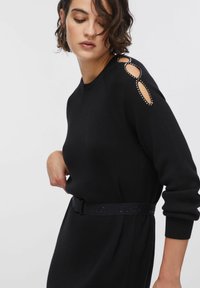 Robe-pull noire avec des détails d'épaule découpés accentués par des clous. Comprend une ceinture noire avec un logo embossé. Texture de tissu douce.