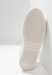 Suela de zapatilla blanca con patrón texturizado y marca. Presenta ranuras para tracción y una forma plana y redondeada. Material de goma suave.