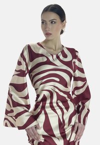 Långärmad klänning med ett mönster i maroon och krämfärgad zebra, tillverkad av glänsande tyg; har en figurnära design med ett brett ärmhål.