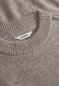 Svetar svetlo rjave boje z ribastim ovratnikom in mehkim otipom. Ima oznako z napisom "GABBA" na ovratniku. Enostaven in klasičen dizajn.