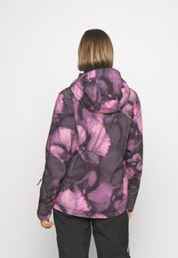 Woman wearing a purple and pink floral patterned hooded jacket, standing facing away against a plain white background.