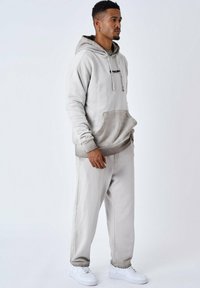 Lichtgrijze hoodie met een voorzak, trekkoorden en geribde manchetten, gecombineerd met bijpassende joggers en witte sneakers. Zachte katoenmix.