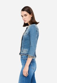 Jeans jakna svetlo modre barve s tremi četrtinami rokavi, raztrganim robom, sprednjimi žepi in okrasnim verižnim dodatkom na manšetah.