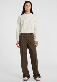 Maglione bianco a collo rotondo con lavorazione a maglia, abbinato a pantaloni larghi a vita alta marroni e sneakers bianche con dettagli marroni.