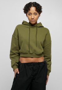 Olive green cropped hoodie with drawstring, relaxed fit, and long sleeves, paired with black loose-fitting pants. Smooth texture, minimal design.