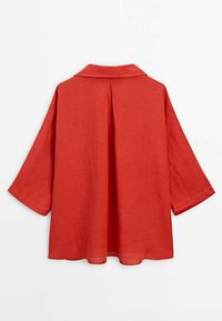 Chemise en lin rouge avec un col à revers, manches courtes et un pli dans le dos pour un drapé supplémentaire. Texture lisse avec une coupe décontractée.