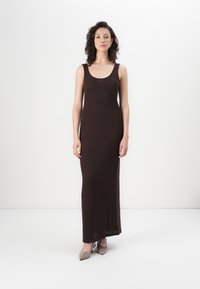 Robe maxi tricotée sans manches de couleur marron, avec un décolleté arrondi et une fente sur le côté, présentant une texture côtelée et une silhouette ajustée.