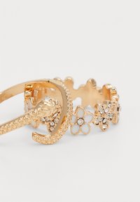 Set di anelli in tono oro con design floreali, dotati di rhinestones incastonati, fascetta testurizzata e motivo serpente. Dettagli notevoli includono strutture aperte e chiuse.