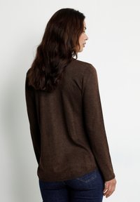 Pull en tricot marron �à manches longues et col rond. Texture douce avec un léger éclat. Porté avec un jean en denim bleu.