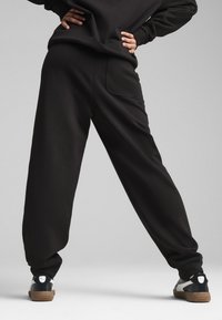 Sorte sweatpants med loose fit, der har en baglomme, diskret tekstureret stof og elastikkanter ved anklerne.