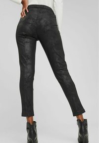 Black faux leather pants with a smooth texture, slim fit, cropped length, and an elastic waistband, paired with ankle boots.