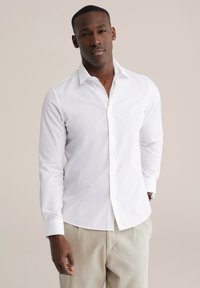 Witte lange mouwen blouse met knopen en een frisse kraag en een gladde textuur, gecombineerd met lichtbeige broek. Eenvoudig ontwerp, zonder patronen.