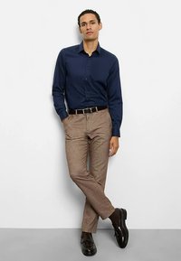 Navyblaues Langarmhemd kombiniert mit hellbraunen, strukturierten Hosen. Accessoires umfassen einen schwarzen Gürtel und glänzende schwarze Schuhe.