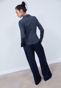 Long-sleeve, collared shirt in dark gray fabric, paired with wide-leg navy pinstriped trousers. Model shown from the back.