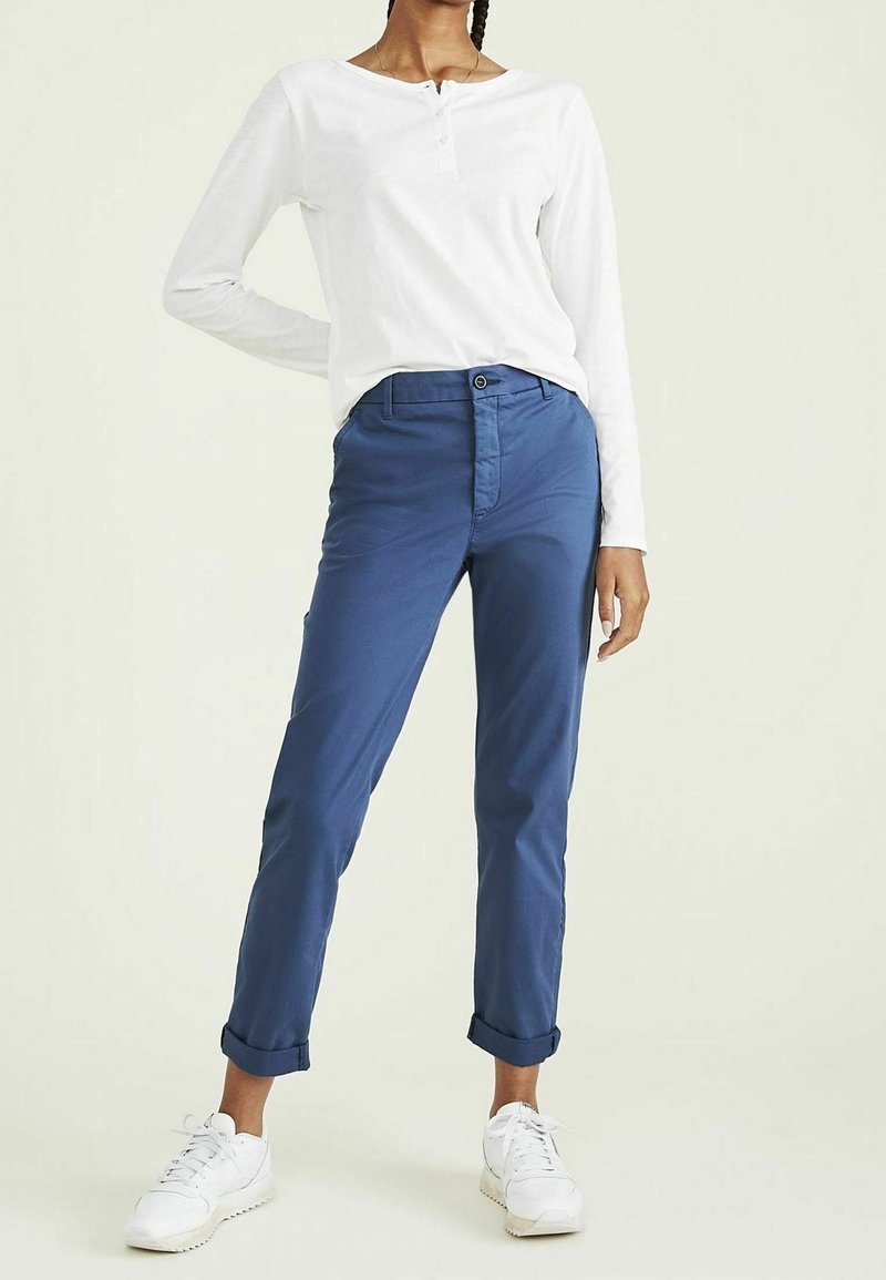 Chemise henley blanche à manches longues avec patte de boutonnage, associée à un pantalon bleu à manches retroussées et des baskets blanches. Tissu doux, coupe ajustée.